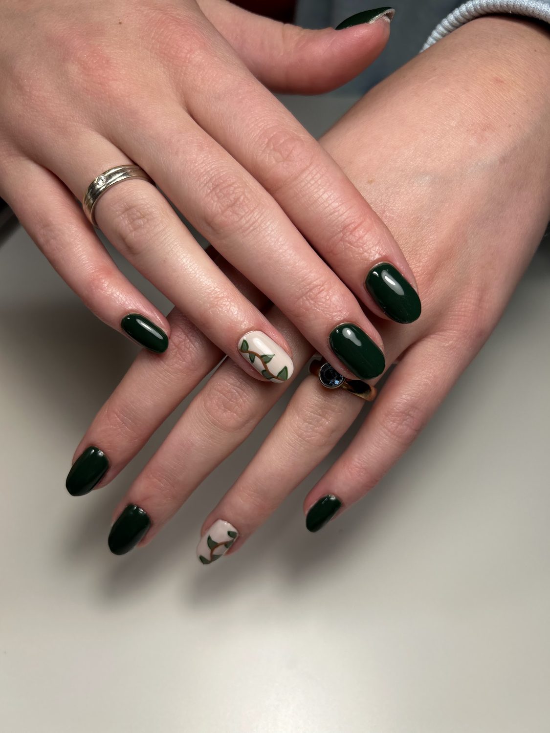 Donkergroene nagels met een paar crèmekleurige nagels met een gouden detail
