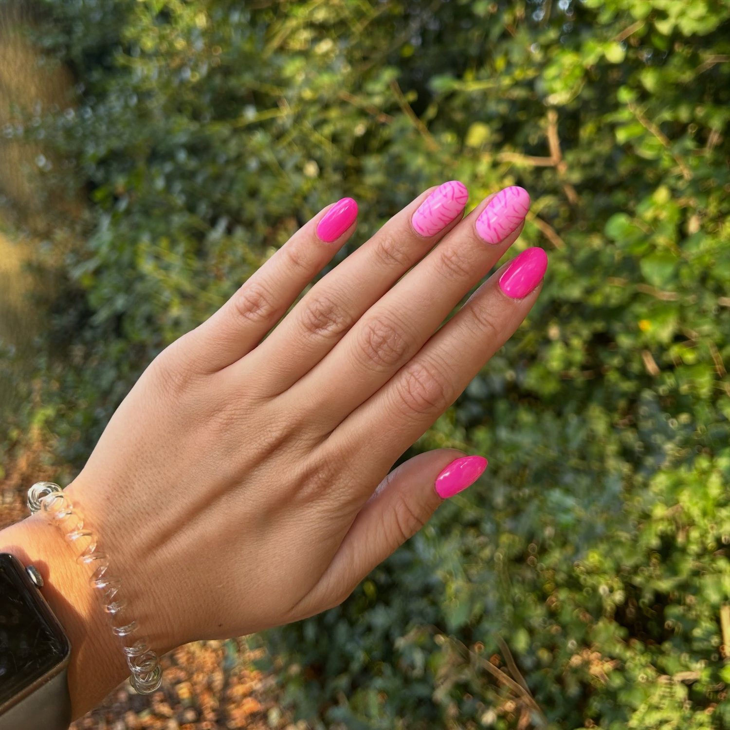 Felroze nagels met één glitternagel tegen groene bladeren